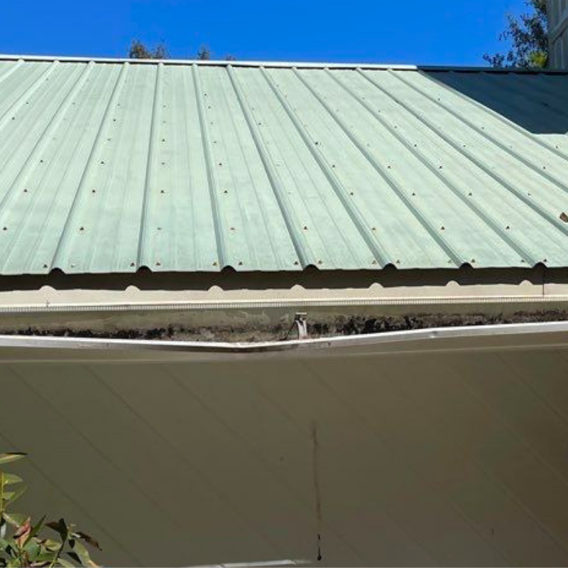 Light green metal roof and damaged white gutter installation on a residential home in Pensacola Florida.