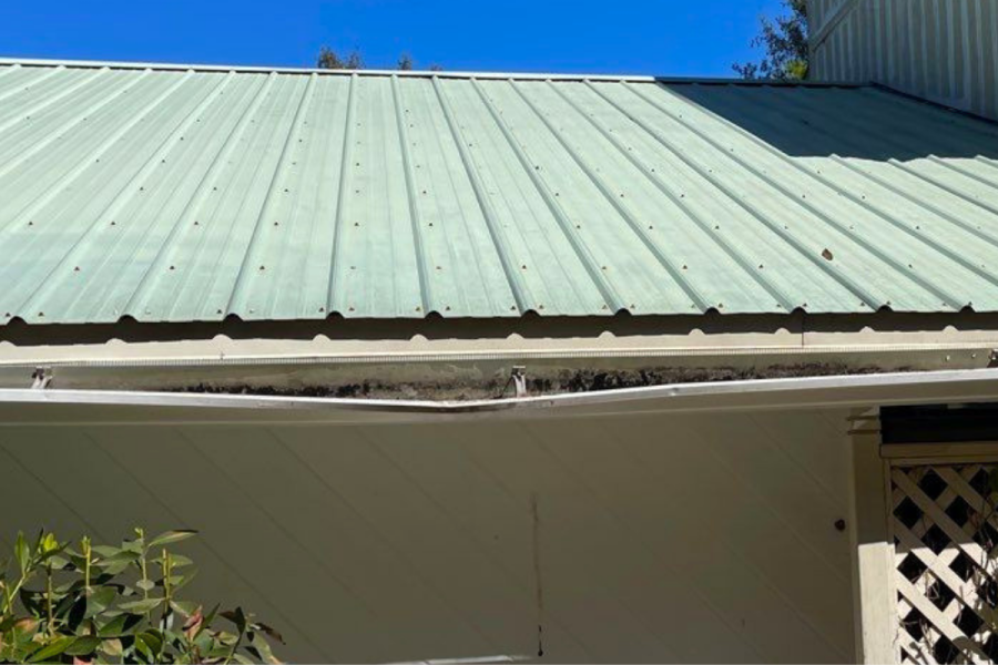 Light green metal roof and damaged white gutter installation on a residential home in Pensacola Florida.